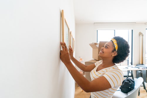 Happy woman hanging a painting on the wall. The best careers for cancer zodiac signs include anythin...