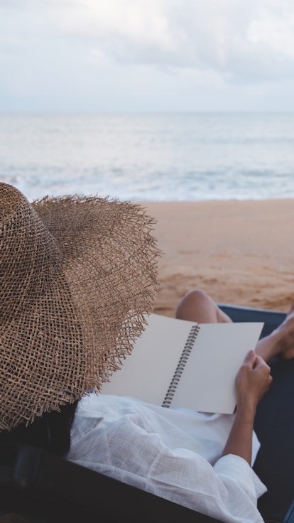 Young beautiful woman sitting on beach reading a book. Beautiful young woman reading e-book while re...