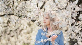 young woman poses under a tree of flowers as she thinks about her june 6, 2022 weekly horoscope
