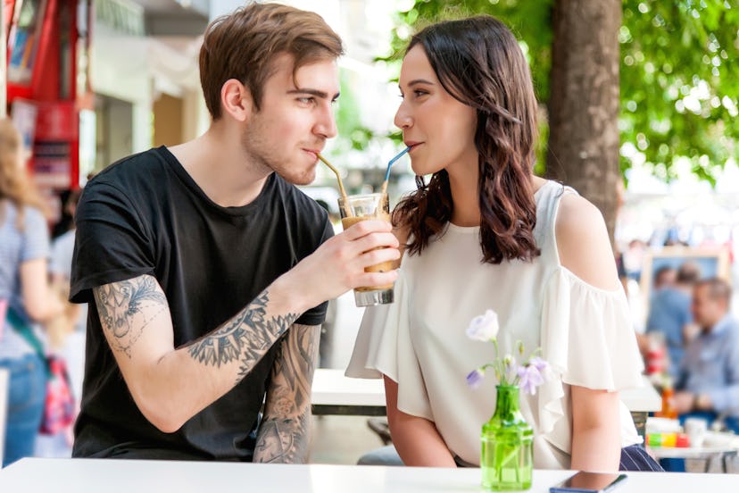 Happy couple sitting on a bench and drinking from one cup.