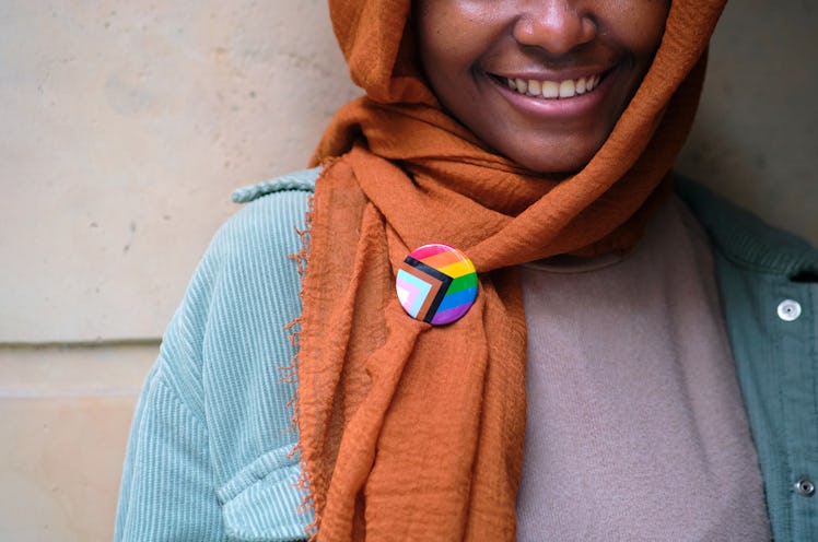 A smiling Muslim woman who is exploring her sexuality wears an LGBTQ pin
