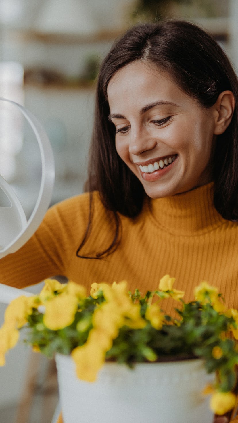 Young woman watering and planting flowers at home