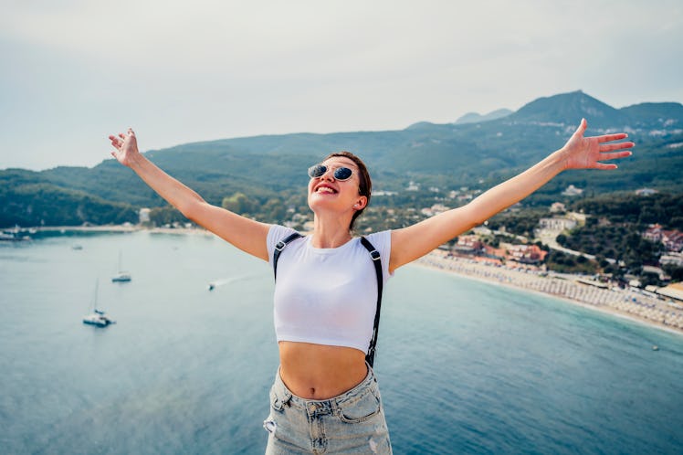 young woman opens arms up wide as she enjoys her vacation and thinks about her june 13, 2022 weekly ...