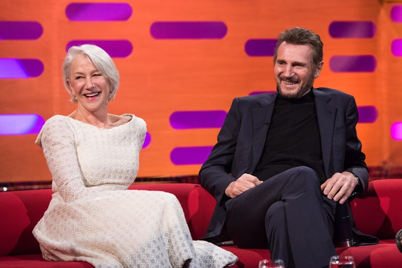 Helen Mirren and Liam Neeson sise side by side on a red sofa against a pink and orange backdrop. Nee...