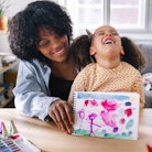 Portrait of an Afro-American family. Mother and daughter proudly showing their colourful drawing.