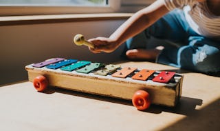 Young child holding a yellow topped beater and playing a colourful old xylophone. Shadows and light ...