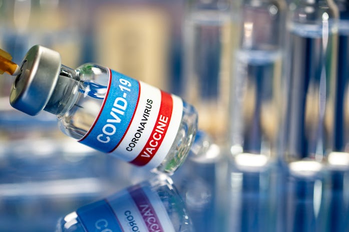 Indoor close up shot of vaccines with syringe, vial and ampules placed on a reflective colored surfa...