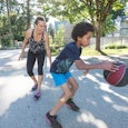A boy is dribbling a basketball while his mom marks him from behind