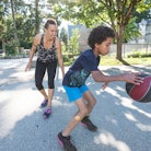 A boy is dribbling a basketball while his mom marks him from behind