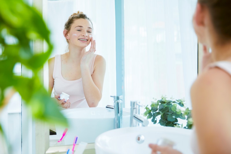 Beautiful teenager putting on face cream in the bathroom