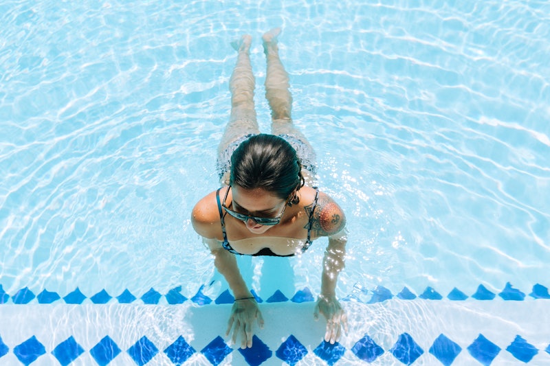 Portraits of a young woman with a shoulder tattoo wading in a swimming pool.