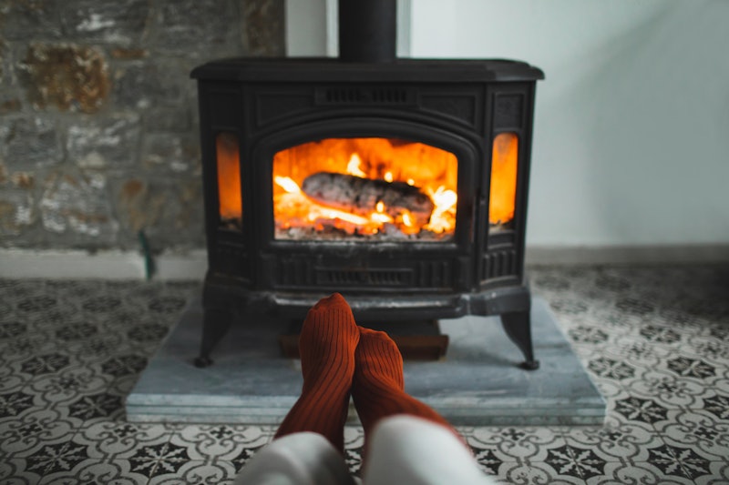 Feet in red socks by the burning fireplace. Family relaxes by warm fire and warming up theirs feet i...