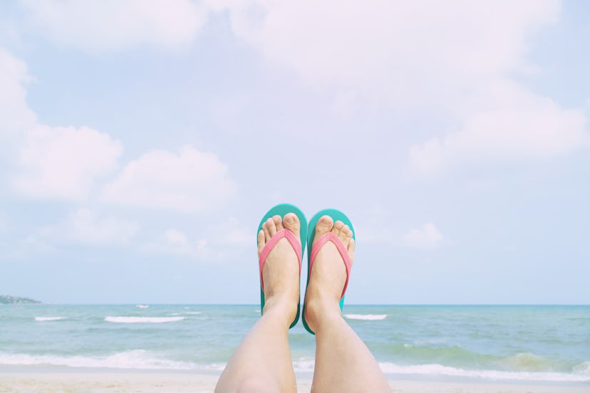 Young people wear the shoes sandals closeup show feet relaxing on beach on sand enjoying chill sun o...