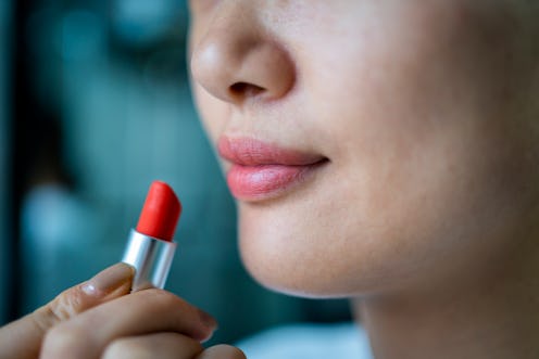 A young woman is putting on lipstick