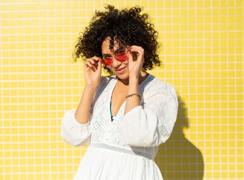 Young woman, wearing heart shaped sunglasses and a white dress, against a yellow background needs Ju...