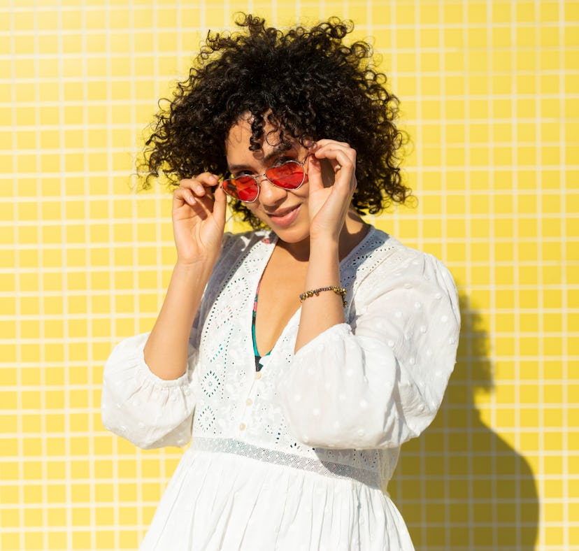 Young woman, wearing heart shaped sunglasses and a white dress, against a yellow background needs Ju...