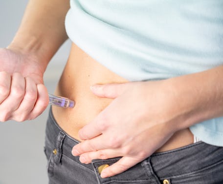 Close-up of a woman's hands and stomach giving herself an insulin injection.