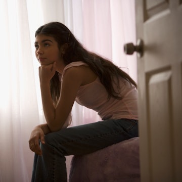 A teen girl sitting on her bed with the bedroom door in frame. A dad just took to Reddit's AITA to a...