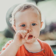 Blue-eyed baby picking his nose while wearing an orange shirt