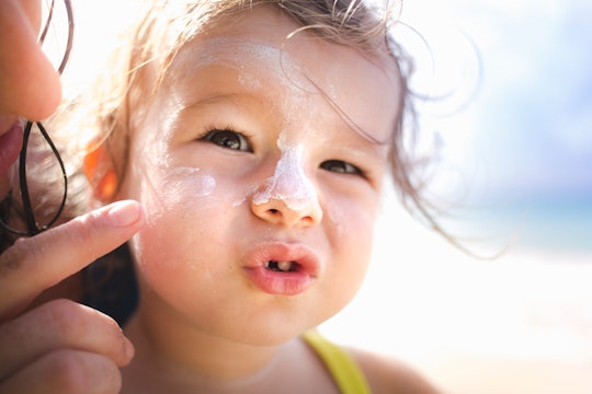 little girl getting sunblock put on her face, the safest sunscreens for children according to the ew...