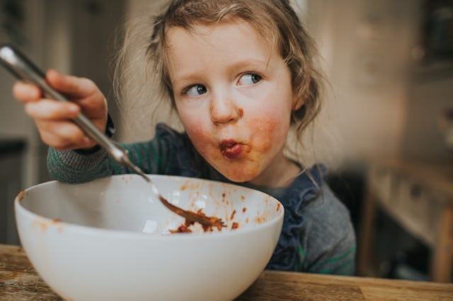 Cute young girl messily eating a big white bowl of Spaghetti Bolognese.
