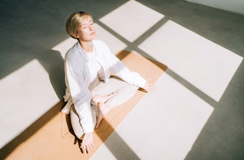 Beautiful authentic woman with short blond hair is meditating sitting in lotus position on yoga mat ...