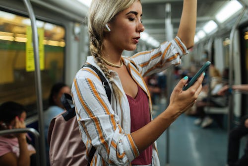 Young blond woman standing in a subway train screenshotting instagram stories.   Does Instagram Tell...