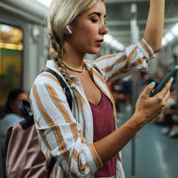 Young blond woman standing in a subway train screenshotting instagram stories.   Does Instagram Tell...