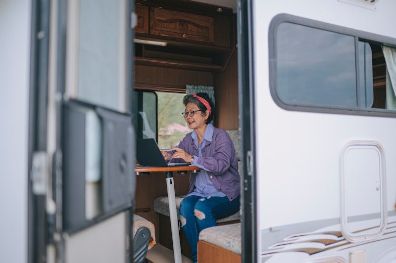 asian chinese senior woman typing on laptop in campervan in the morning during vacation