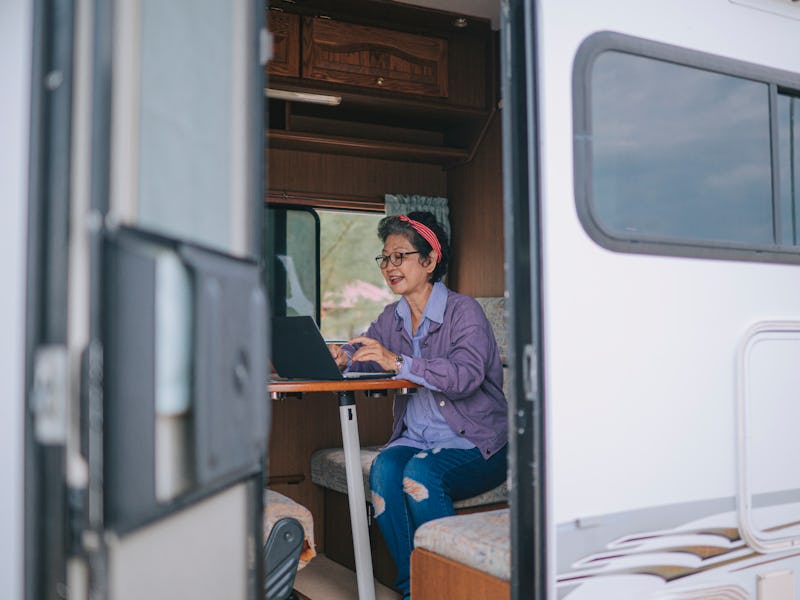 asian chinese senior woman typing on laptop in campervan in the morning during vacation