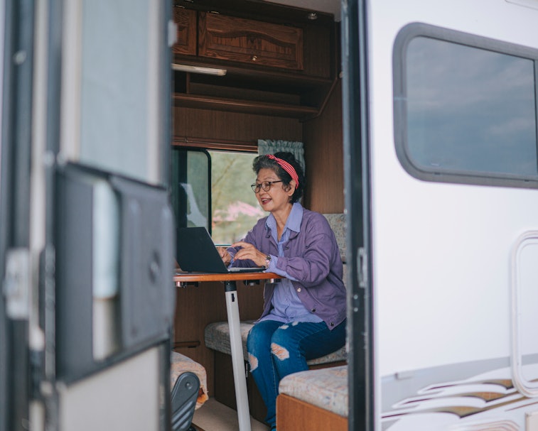 asian chinese senior woman typing on laptop in campervan in the morning during vacation