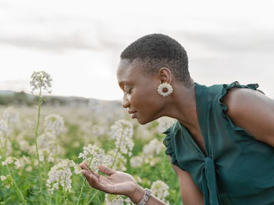 Portrait of beautiful woman smelling white flowers on field enjoying spring day outdoors