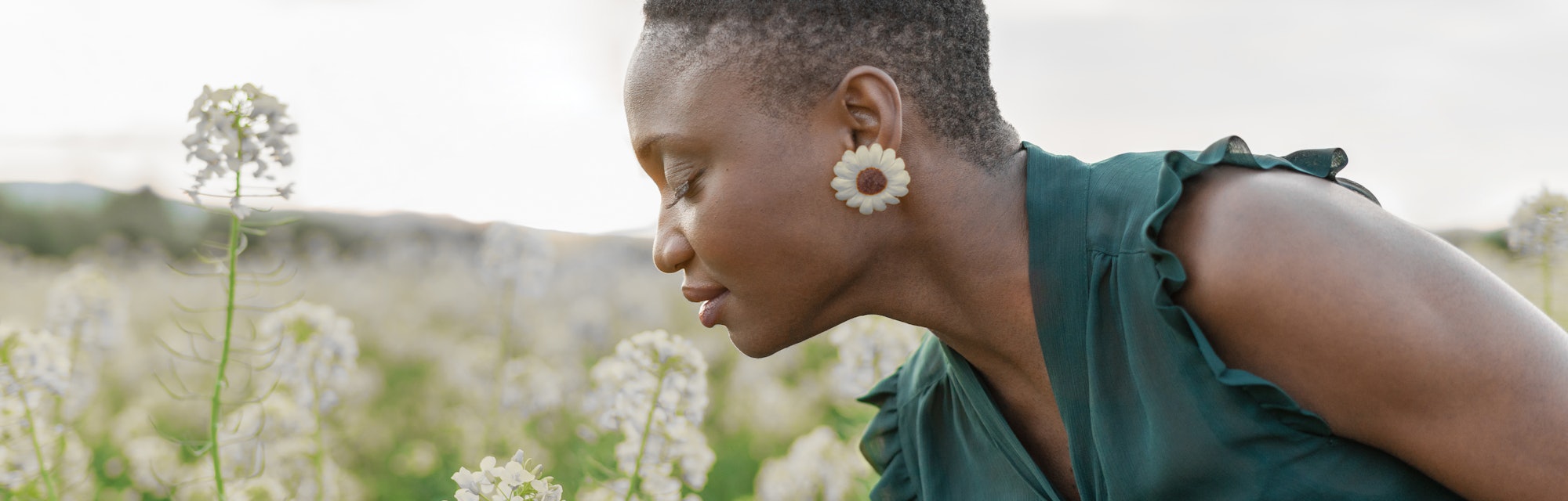 Portrait of beautiful woman smelling white flowers on field enjoying spring day outdoors
