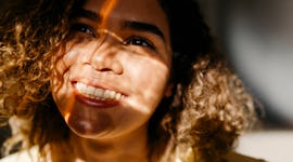 young woman smiles as she looks up at the sun, reflecting on her May 30, 2022 weekly horoscope.