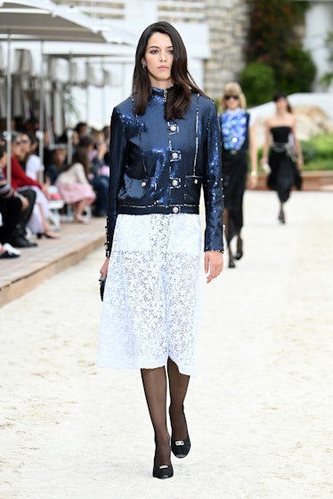 A model walking the runway for the Louis Vuitton's 2023 Cruise Show in a black jacket and white dres...