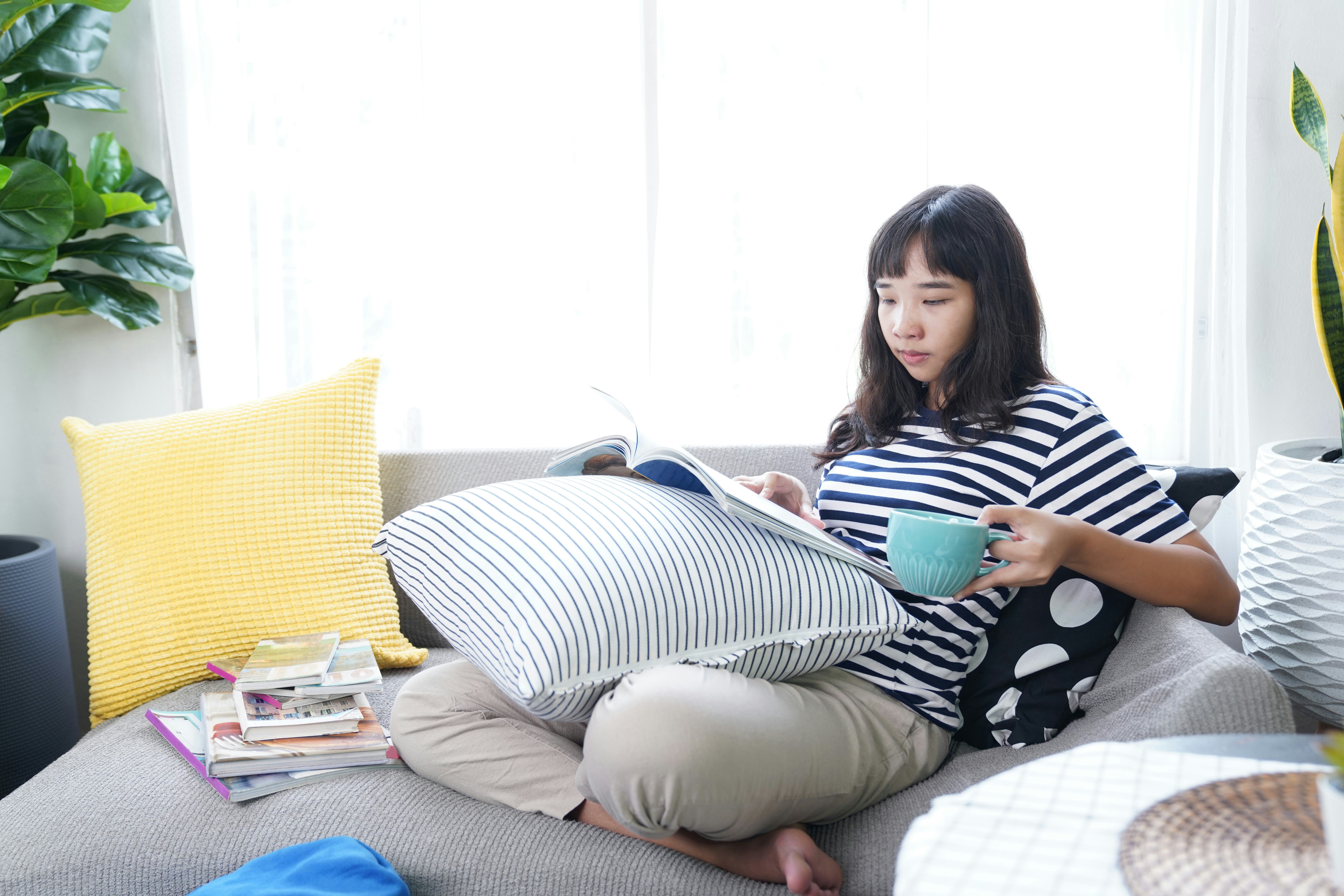 Young woman sitting on sofa reading magazine and drink coffee leisure activity in weekend