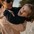 Close-up shot of mother holding laughing little daughter and spinning on sandy beach on their vacati...