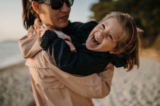 Close-up shot of mother holding laughing little daughter and spinning on sandy beach on their vacati...