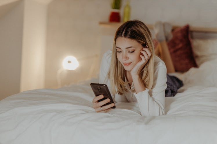 Gen Z woman lying stomach down in her bed, sending dirty text to her partner before bed