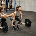 Athletic woman weightlifting working out in gym with coach or instructor