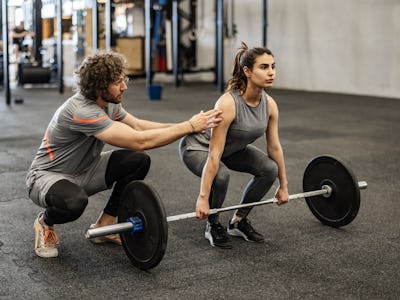 Athletic woman weightlifting working out in gym with coach or instructor