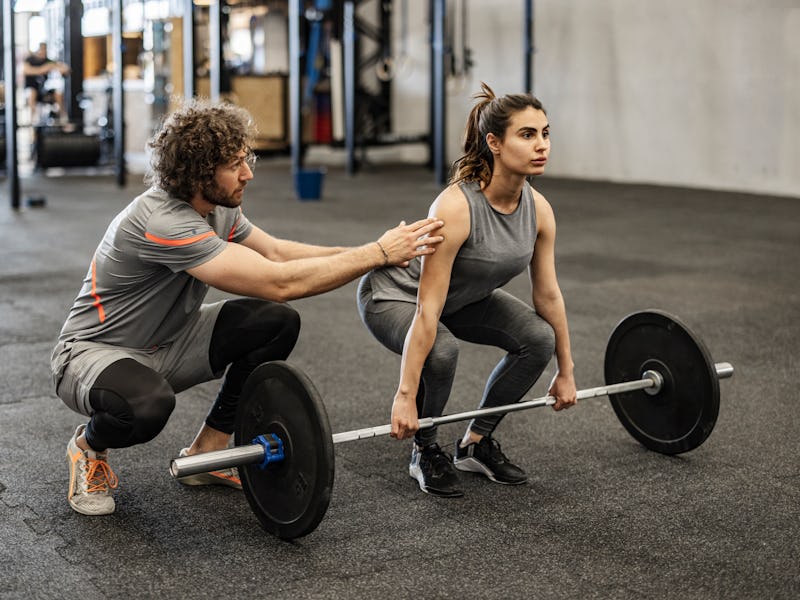 Athletic woman weightlifting working out in gym with coach or instructor