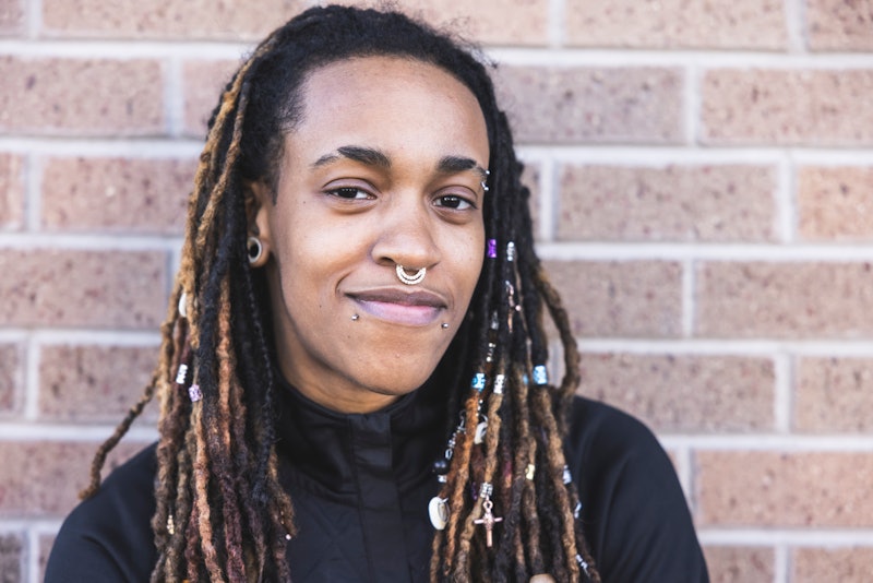 A portrait of an androgynous African American person on a brick background.