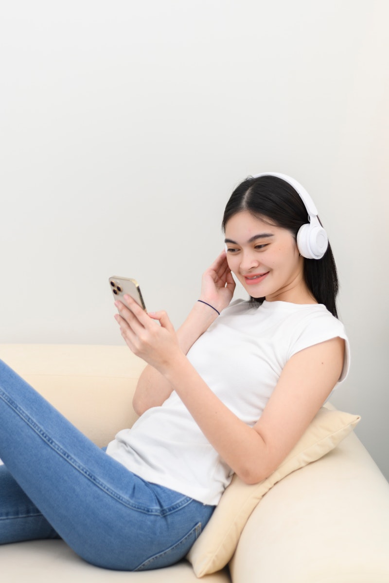 Young woman wearing headphones listening music from smart phone on sofa