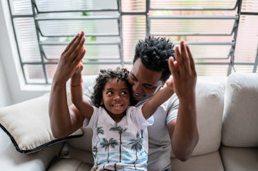 A boy sits on his dad's lap on a couch as they talk.