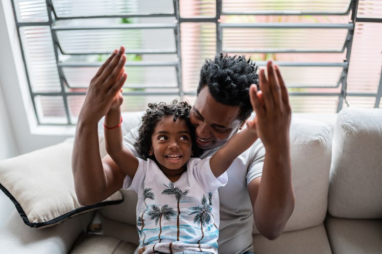 A boy sits on his dad's lap on a couch as they talk.