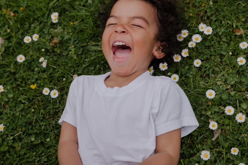 Little boy with a Roman baby names lies on a field with daisies and laughs