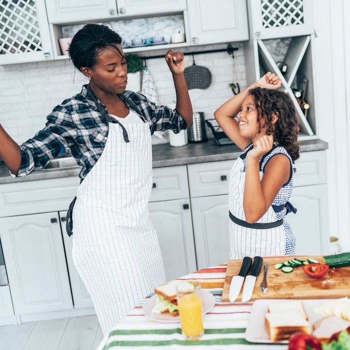 Mixed race mother and daughter dancing while cooking together in the kitchen