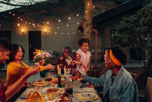 African american multi-generation family having dinner outdoors in their back yard, celebrating with...