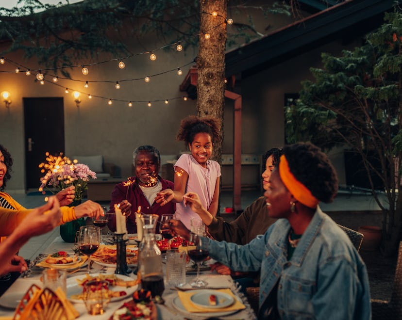 African american multi-generation family having dinner outdoors in their back yard, celebrating with...